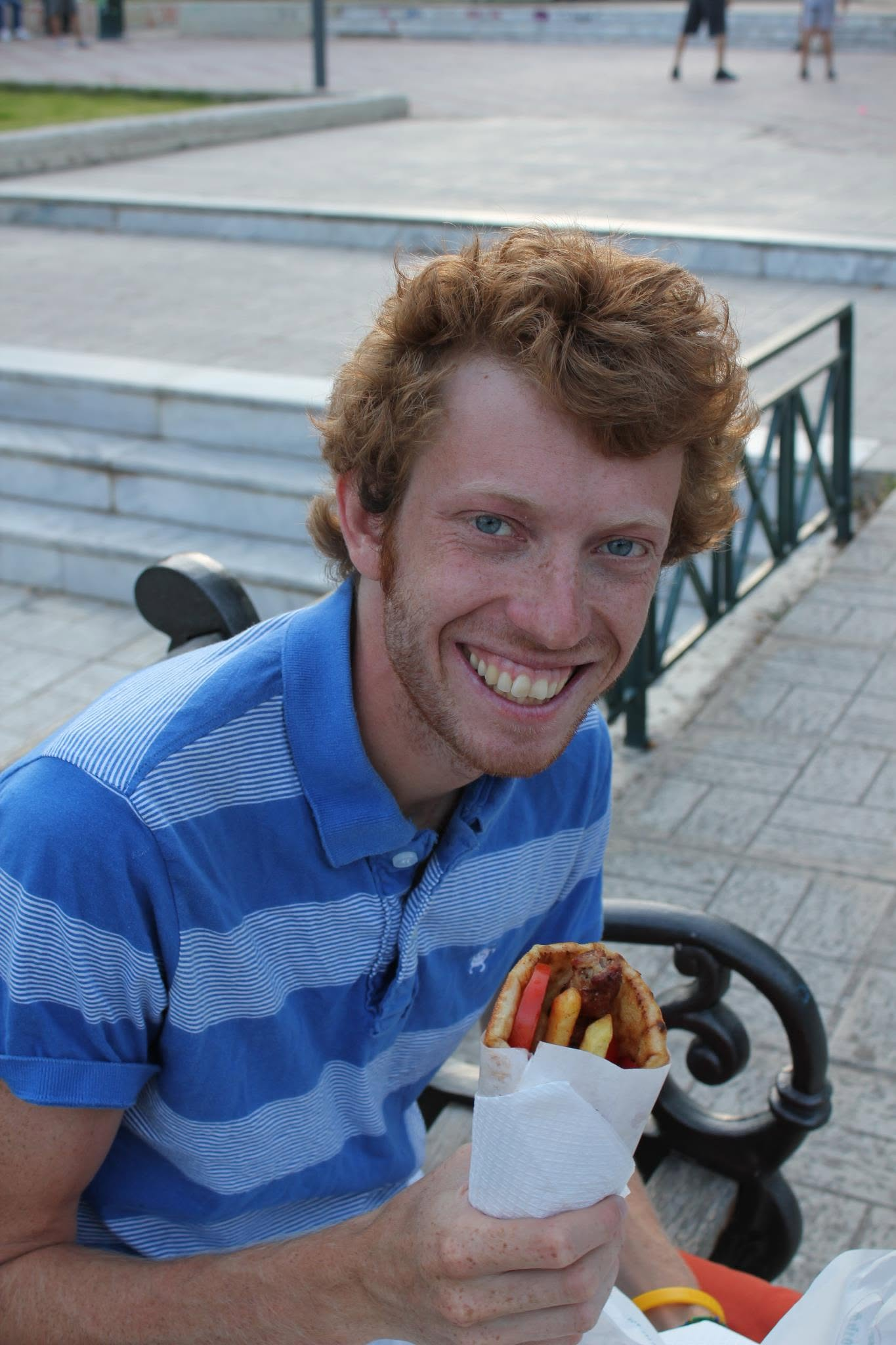 The person behind Chapko, smiling outdoors and holding a sandwich.